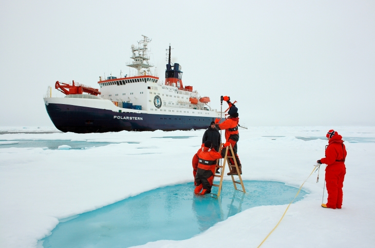 Scientists measure the thickness of the sea ice with ice drills, in the background the Polarstern